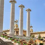 Τέσσερις μεγάλες κολώνες με γλυπτά και σκαλιά, μπροστά από ένα κτίριο με περίτεχνη διακόσμηση και καθαρό ουρανό στο φόντο