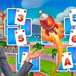 Μια ξανθιά γυναίκα χαμογελάει και κρατά ένα μικρό ρουκέτα, με φόντο κάρτες και εξωτερικό χώρο κτιρίου