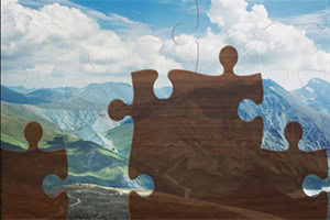 Κομμάτια παζλ σε πρώτο πλάνο με φόντο ένα ορεινό τοπίο και συννεφιασμένο ουρανό